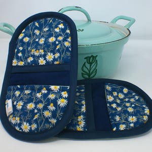 May include: A pair of blue and white pot holders with a floral pattern. The pot holders have a dark blue border and a pocket on the back.