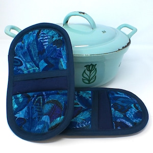 Könnte beinhalten: Zwei blaue Ofenhandschuhe mit Federmuster und ein passender hellblauer Topf. Die Handschuhe haben eine dunkelblaue Paspel und ein dunkelblaues Band in der Mitte. Der Topf hat ein grünes Blumendesign.