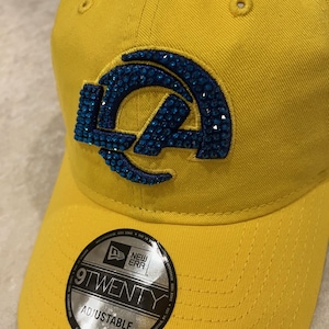 May include: A yellow adjustable baseball cap with a blue jeweled logo. The cap features the text "9TWENTY ADJUSTABLE" on a circular sticker. The hat is made of a durable fabric.