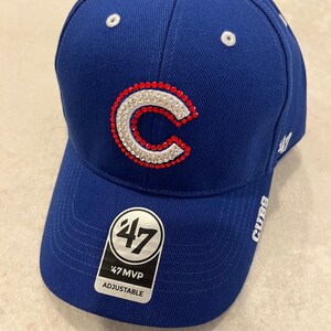 May include: Royal blue adjustable baseball cap with a white and red jeweled "C" logo. The cap has a curved brim and a white button on top. The tag reads "47 MVP ADJUSTABLE". The word "CUBS" is printed on the side.
