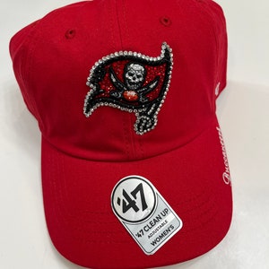 May include: Red baseball cap with a rhinestone embroidered Tampa Bay Buccaneers logo. The cap has a 47 Brand logo and says "47 Clean Up Adjustable Women's".