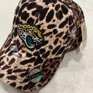 May include: Leopard print baseball cap with a distressed design. Features a patch of a jaguar with gold and teal accents. The cap has a curved brim and a tag that reads "Vintage Since 2001".