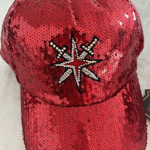 May include: A red sequined baseball cap with a large, silver starburst design in the center.
