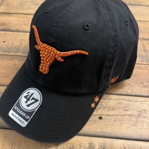 May include: Black adjustable baseball cap with a sparkling orange Longhorn logo. The cap features the "47 Clean Up" tag and additional orange embellishments. A stylish accessory for fans.