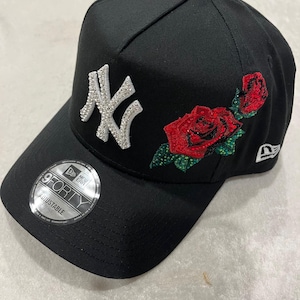 May include: Black baseball cap with a white rhinestone New York Yankees logo and red rhinestone roses on the side. The cap is adjustable and has a 9FORTY label.