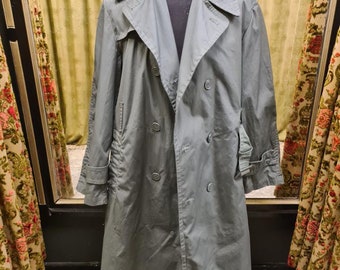 May include: A long, green, double-breasted trench coat with a belt. The coat has a classic design and is made of a durable fabric.