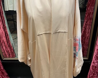 Könnte beinhalten: Ein langer, blassrosa Kimono mit einem Blumenmuster auf dem rechten Ärmel. Der Kimono ist aus seidenartigem Stoff gefertigt und hat einen weiten, offenen Kragen.