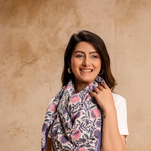 Op de afbeelding: Een vrouw draagt een wit T-shirt en een blauwe jeans en een witte en blauwe bloemenprint sjaal om haar nek. De sjaal heeft roze bloemen en blauwe bladeren.