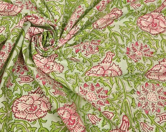Op de afbeelding: Een witte stof met een groene en roze bloemenprint. De stof is gevouwen en laat het patroon zien.