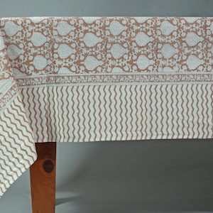 May include: A brown and white cotton tablecloth with a floral pattern and a wavy border. The tablecloth is draped over a wooden table.