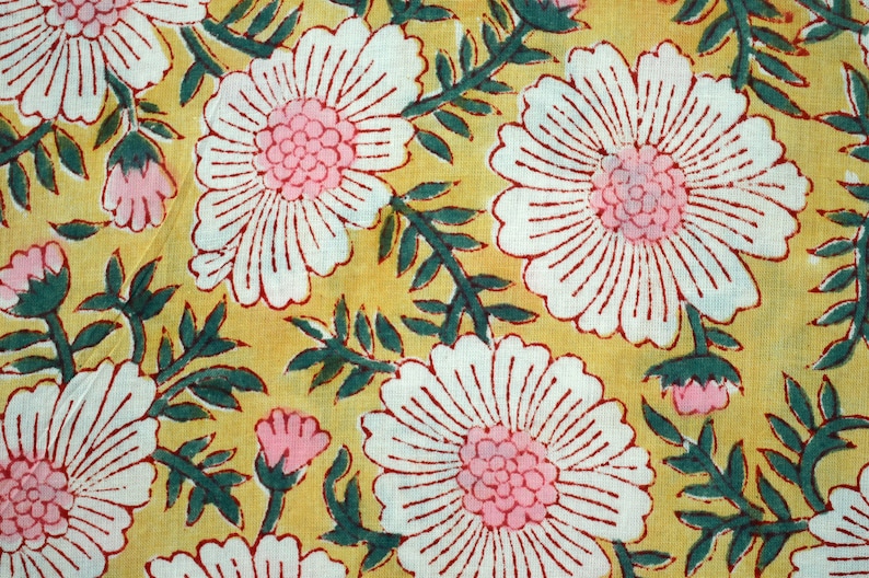 May include: A yellow fabric with a white and red floral pattern. The flowers are stylized and have a pink center.