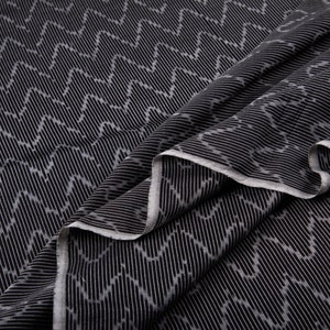 May include: Black fabric with a white chevron pattern. The fabric is folded and draped, showing the texture and pattern.