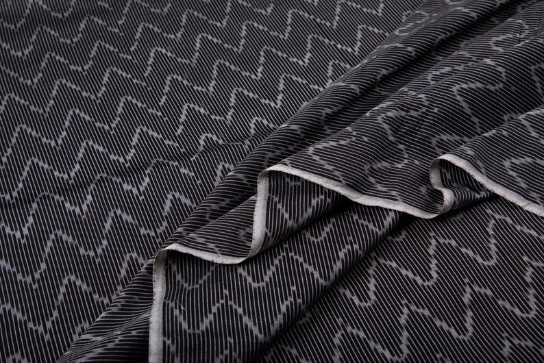 May include: Black fabric with a white chevron pattern. The fabric is folded and draped, showing the texture and pattern.