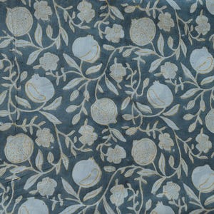 May include: A close-up of a fabric with a repeating pattern of white pomegranates, flowers, and leaves on a teal background. The design has a vintage, botanical aesthetic, with a slightly faded appearance.