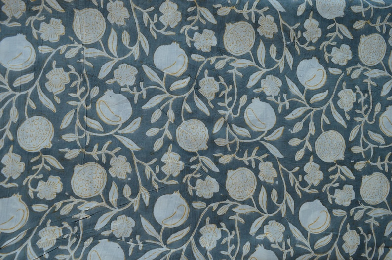 May include: A close-up of a fabric with a repeating pattern of white pomegranates, flowers, and leaves on a teal background. The design has a vintage, botanical aesthetic, with a slightly faded appearance.