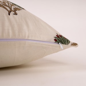 May include: Cream-colored decorative pillow with a floral pattern in shades of green, red, and brown. The pillow has a zipper closure and is made of a soft fabric. The pillow is designed for home decor.