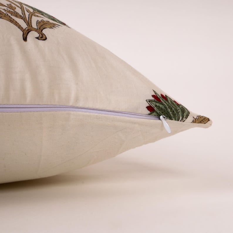 May include: Cream-colored decorative pillow with a floral pattern in shades of green, red, and brown. The pillow has a zipper closure and is made of a soft fabric. The pillow is designed for home decor.
