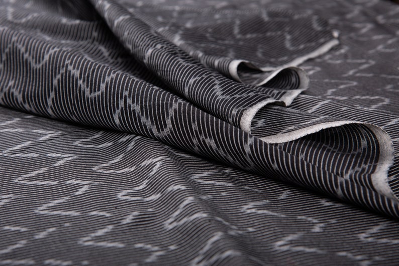 May include: Black and white striped fabric with a subtle pattern. The fabric is folded and draped, showing the texture and weave.