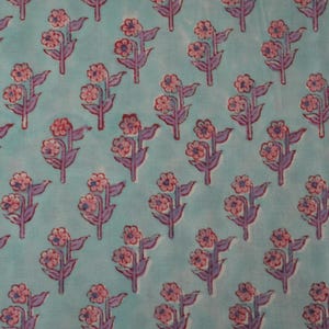 May include: A repeating pattern of pink flowers with purple stems and leaves on a light blue background. The floral design is evenly spaced across the fabric, creating a visually appealing textile pattern. The flowers have multiple petals.