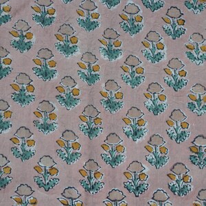 May include: A repeating pattern of stylized floral designs on a pink fabric. Each flower has a beige bloom, yellow center, and green leaves. The fabric is likely cotton or linen.