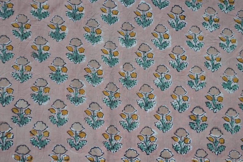 May include: A repeating pattern of stylized floral designs on a pink fabric. Each flower has a beige bloom, yellow center, and green leaves. The fabric is likely cotton or linen.