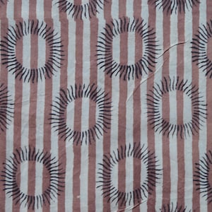 May include: A close-up of a fabric with a repeating pattern. The design features alternating vertical stripes in white and a muted reddish-brown colour. Within the stripes are circular motifs with a sunburst-like design in a darker shade of brown.