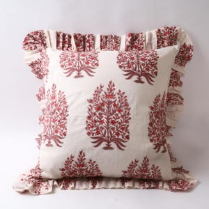 May include: A square cushion with a cream background featuring a repeating pattern of red floral tree designs. The cushion has a ruffled edge in the same red and cream pattern.