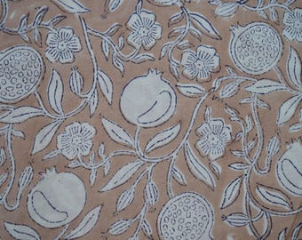 May include: Tan fabric with a repeating pattern of white pomegranates, flowers, and leaves. The design features detailed outlines in a dark blue color, creating a contrasting effect against the tan background. The floral elements are stylized.