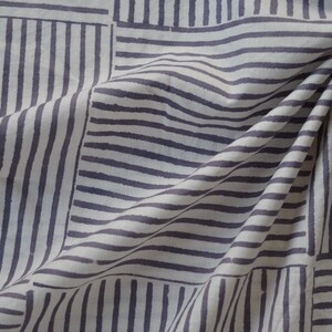 May include: White fabric with a geometric pattern of gray stripes. The fabric is folded and draped, showing the pattern from different angles.
