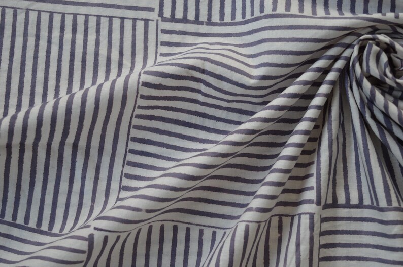 May include: White fabric with a geometric pattern of gray stripes. The fabric is folded and draped, showing the pattern from different angles.