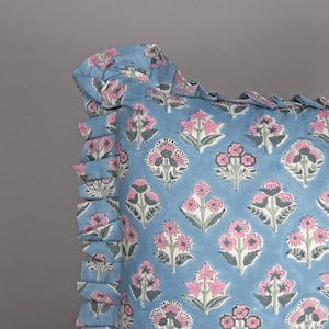 Könnte beinhalten: Ein blaues Kissen mit einem floralen Muster in Rosa- und Grüntönen. Das Kissen hat einen gekräuselten Rand.