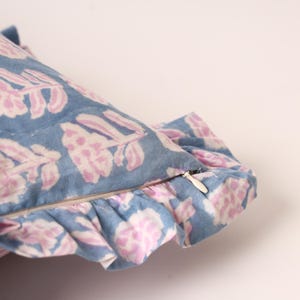 Könnte beinhalten: Ein blaues Zierkissen mit einem floralen Muster in Rosa und Weiß. Das Kissen hat einen gerüschten Rand und einen Reißverschluss. Das Kissen ist für die Inneneinrichtung bestimmt.