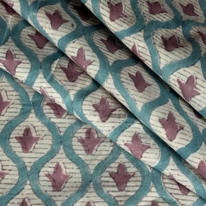 Könnte beinhalten: Tealfarbener Stoff mit einem sich wiederholenden geometrischen Muster in Mauve. Der Stoff hat eine weiche, fließende Textur.