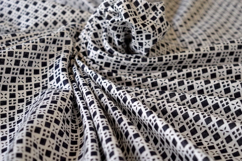 May include: White fabric with a black geometric pattern. The fabric is folded and draped, creating a swirling effect.