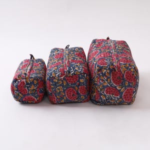 Può includere: Tre borse da viaggio trapuntate di diverse dimensioni. Le borse presentano un motivo floreale con fiori rossi e foglie gialle su sfondo blu navy. Ogni borsa ha una chiusura con cerniera.