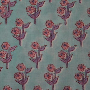 May include: A repeating pattern of stylized flowers on a light blue background. The flowers are pink with purple stems and leaves. The fabric has a soft, slightly faded appearance, suggesting a vintage or handmade quality.