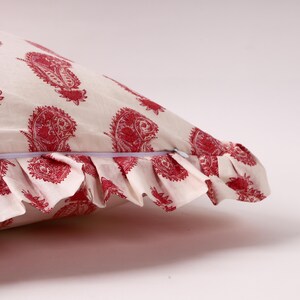 May include: A white pillow with a red paisley print and a ruffled edge. The pillow has a zipper closure.