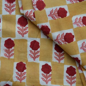 May include: A textile fabric featuring a repeating pattern of dark red floral motifs printed on alternating rectangular blocks of mustard yellow and white. The design displays a consistent grid-like arrangement of flowers with stems and leaves.