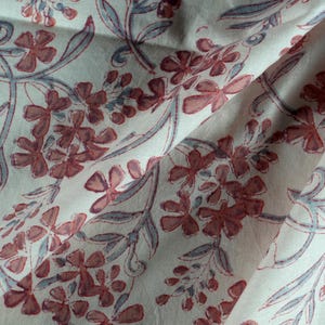 Pode incluir: Tecido branco com um padrão floral. As flores são de cor rosa claro e as folhas são de cor cinza claro.