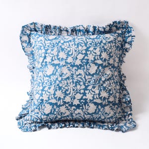 Peut inclure: Coussin carré avec un motif floral bleu et des bords à volants. Le coussin présente un motif floral blanc détaillé sur un fond bleu. La bordure à volants ajoute une touche décorative au design du coussin.