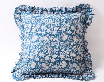 May include: Square throw pillow with a blue floral pattern and ruffled edges. The pillow features a detailed white floral design on a blue background. The ruffled border adds a decorative touch to the pillow's design.