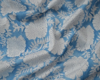 May include: Light blue fabric with a repeating pattern of large white floral designs and smaller leaf accents. The fabric is soft and appears to be cotton or a similar material, with visible folds and creases.