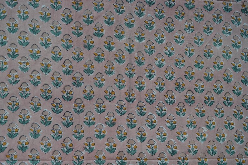 May include: A fabric with a repeating floral pattern. The flowers are yellow and gray with teal green leaves, set against a pale pink background. The design is evenly spaced across the fabric.