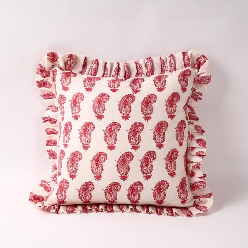 May include: A white pillow with a red paisley pattern and a ruffled border.