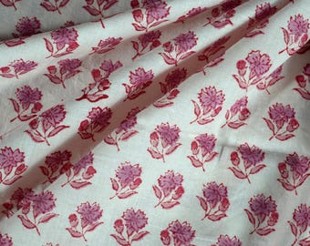May include: White cotton fabric with a repeating pattern of pink floral designs. The fabric is folded and draped, showing the pattern.