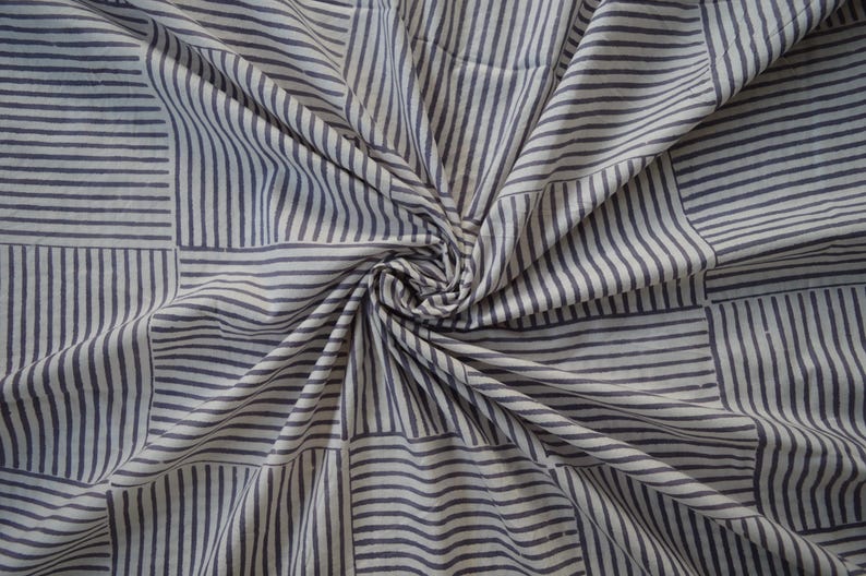 May include: White fabric with a blue and white striped pattern. The fabric is folded and twisted, creating a swirling effect.