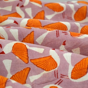 以下が含まれることがあります： 薄い紫色の背景に、オレンジと白のスタイリッシュな鳥が繰り返しパターンで描かれた布のクローズアップ。