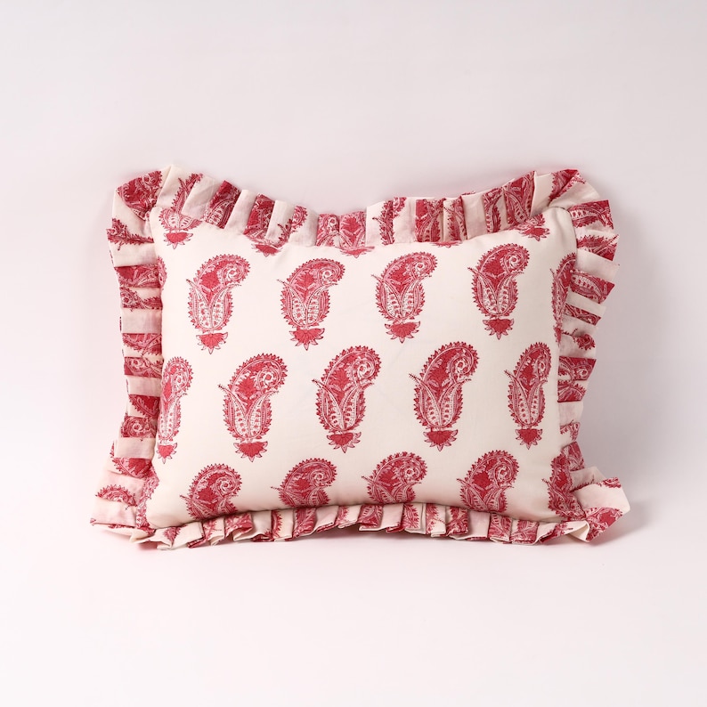 May include: A white pillow with a red paisley pattern and a ruffled border.