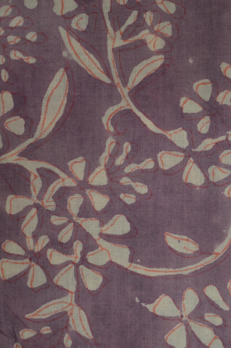 Op de afbeelding: Paarse stof met een wit bloemenpatroon. De bloemen zijn omrand met een licht oranje kleur.