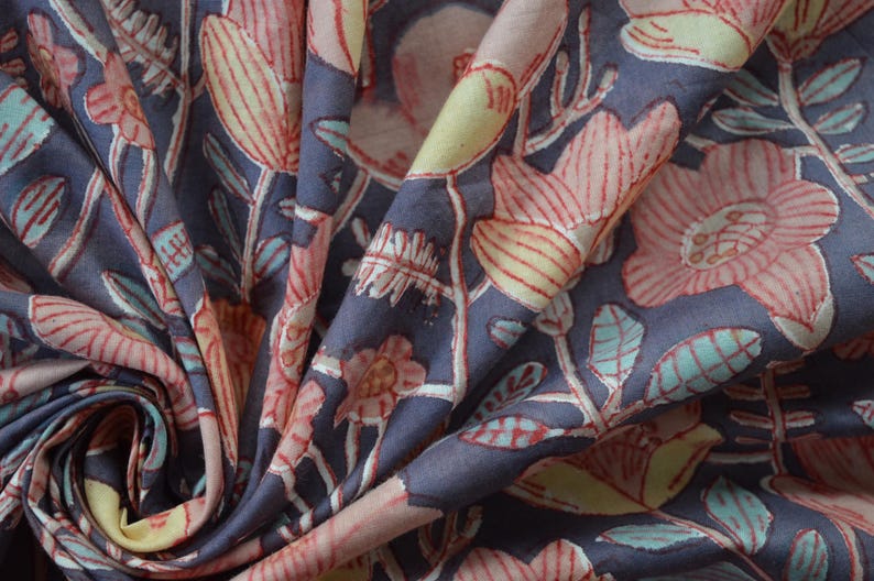 Pu&ograve; includere: Primo piano di un tessuto blu con stampa floreale. Il tessuto &egrave; decorato con fiori e foglie rosa, gialli e bianchi.